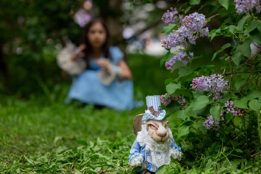 White rabbit figurine in garden with young caucasian girl in background.