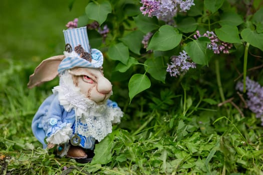 Decorative white rabbit figurine in blue victorian outfit amidst lilac flowers.