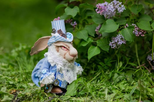 Steampunk rabbit figurine in blue attire with lilac flowers in garden.