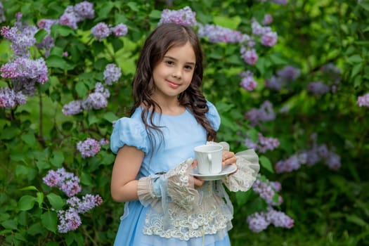 Young caucasian girl in blue dress holding teacup in garden.