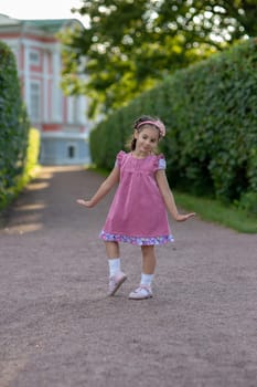 Young caucasian girl in pink dress dancing on pathway in summer garden.