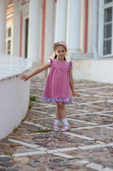Young caucasian girl in pink dress posing outdoors on cobblestone path.