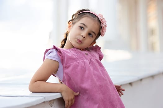 Playful young girl posing outdoors in pink dress.