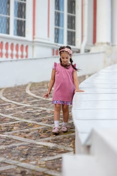 Young girl in pink dress walking on cobblestone path in front of vintage building.