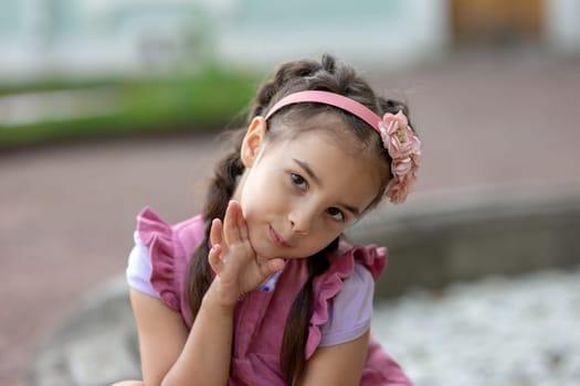 Young caucasian female child in pink dress with flower headband smiling playfully outdoors.