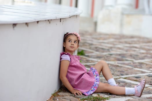 Young girl in pink dress sitting on cobblestone street.