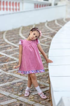 Young caucasian female child in pink dress standing on steps outdoors.