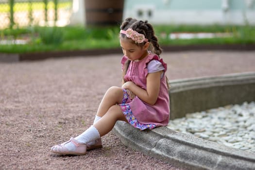 Young caucasian girl in pink dress sitting by garden fountain thoughtfully.