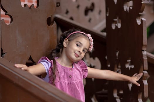 Cute young girl in pink dress smiling on wooden playground structure.