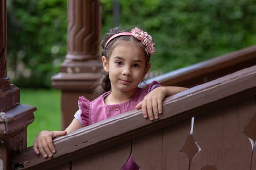 Young caucasian girl with pink headband posing on wooden staircase outdoors.