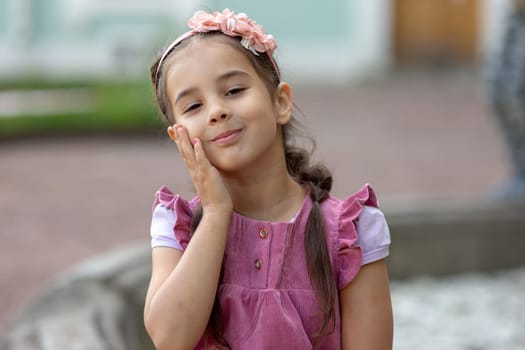 Cute young girl smiling outdoors with flower headband and pink dress.