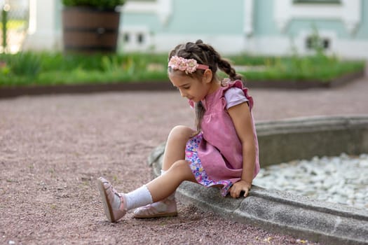 Young girl sitting by fountain in pink dress outdoors.