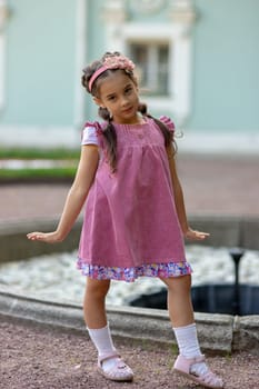 Young caucasian girl in pink dress posing outdoors near fountain.