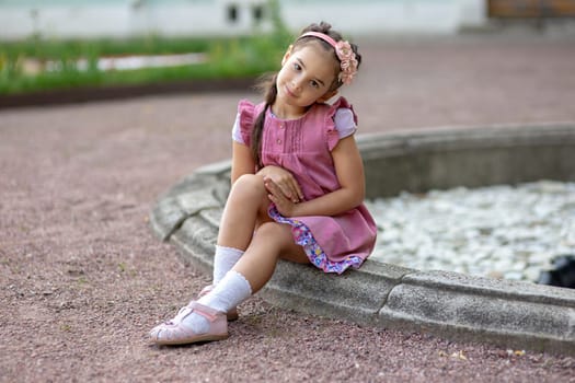 Young caucasian girl in pink dress sitting by fountain in garden setting.