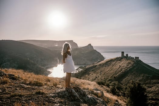 A woman stands on a hill overlooking a body of water. The sky is clear and the sun is shining brightly. The woman is enjoying the view and the peaceful atmosphere