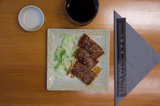 A plate of meat and vegetables sits on a wooden table. A cup of coffee is next to the plate