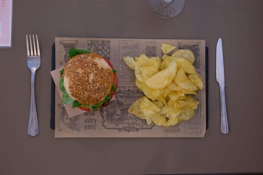 A plate of food with a burger and chips on top of a newspaper. Scene is casual and relaxed, as it is a simple meal with no fancy presentation
