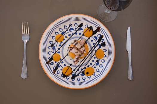 A plate of food with a fork and knife on a table. The plate has a dessert with chocolate sauce on it