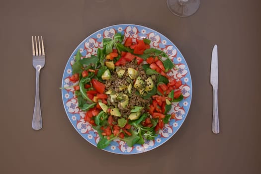 A plate of food with a fork and knife on a table. The plate has a salad with tomatoes and avocado