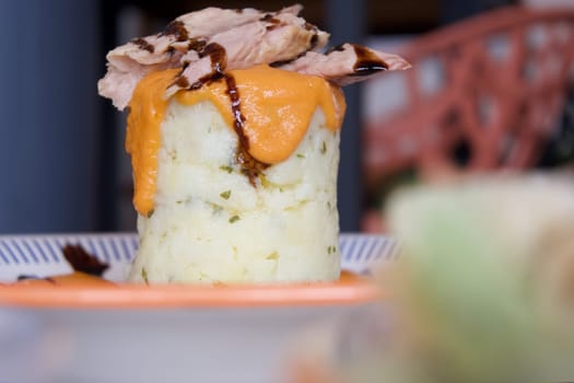 A plate of food with a meaty topping on top of a potato. The plate is on a table