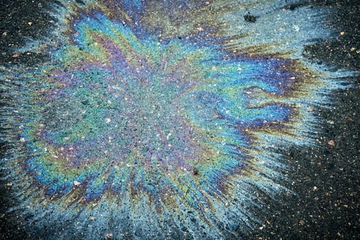 Colorful oil spill generating a vivid rainbow reflection on the dark pavement of the road