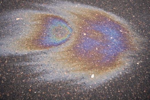 Colorful gasoline or oil spill creating a rainbow sheen on asphalt road surface.