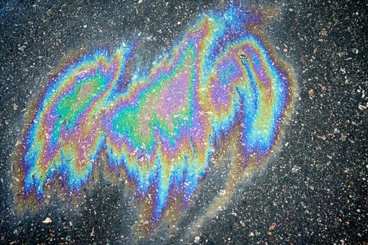 Colorful gasoline or oil spill on asphalt creating rainbow sheen reflecting
