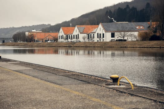 Modern white buildings with red-tiled roofs and solar panels on a riverbank. Their reflection in the calm water enhances the industrial yet serene atmosphere of the scene