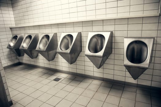 Stainless steel urinals in a modern public restroom with white tiled walls. A clean and industrial design representing hygiene, functionality, and urban infrastructure. Ideal for architectural