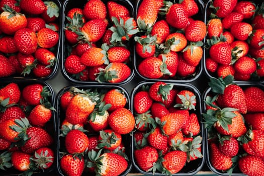 Fresh ripe strawberries in black containers at a market. Vibrant red berries. Ideal for food photography, organic produce, healthy eating visuals, and fruit market scenes
