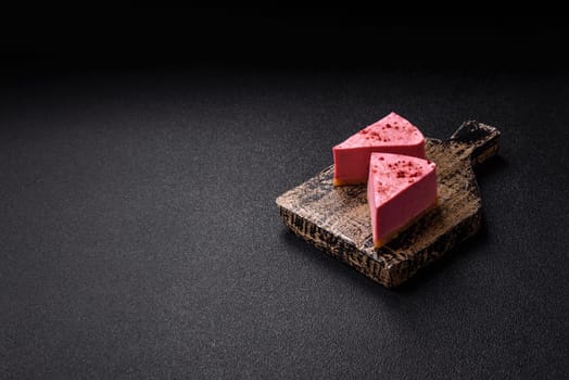 A piece of sweet cheesecake with raspberry or strawberry flavor, with mascarpone cheese on a dark concrete background