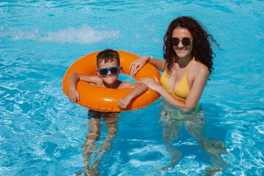 happy young mother teaches child boy son to swim in swimming pool at a hotel on vacation at a resort in the summer