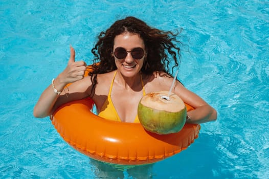 happy young woman in sunglasses with coconut for drinking rests in an inflatable circle in pool at hotel on vacation at resort in the summer