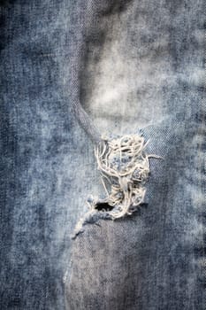 A detailed closeup image of frayed denim fabric showcasing its unique tear along with a wellworn texture
