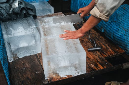 man cuts a block of ice for freezing and cocktails with a saw on street in Asia in Vietnam