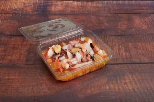 A container of food with a lid on top. The lid is open and the food inside is a mix of seafood and vegetables