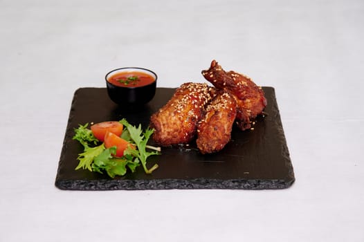 A plate of chicken wings with a side of salad. The chicken wings are seasoned and look delicious. The salad is fresh and colorful, with a variety of greens and tomatoes