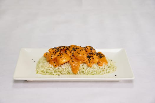 A plate of food with rice and chicken. The rice is brown and the chicken is orange. The plate is white and the food is on a white table