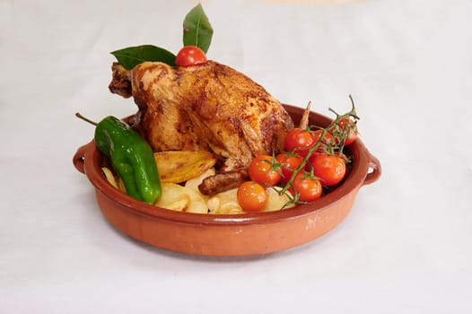 A chicken is sitting on a plate with a tomato and a pepper. The plate is on a white table