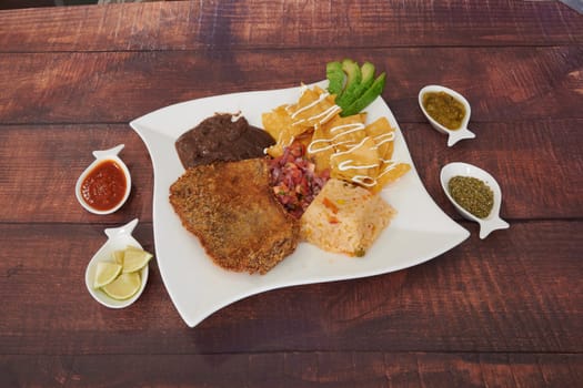 A plate of food with a variety of items including a piece of meat, beans, and tortilla chips