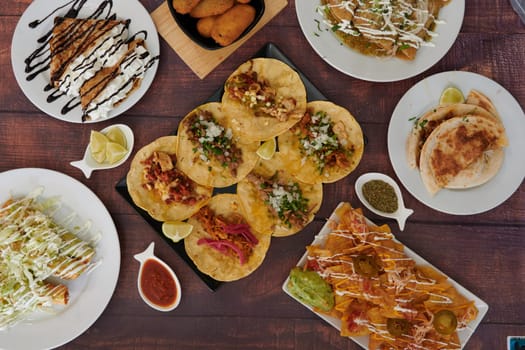 A table full of Mexican food including tacos, nachos, and burritos. The table is set with plates and bowls of food, and there are several spoons and forks. Scene is inviting and delicious