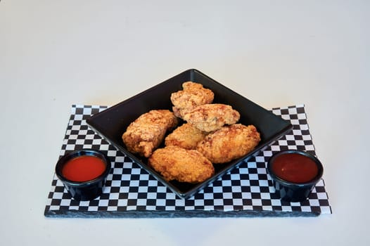 A plate of fried chicken with a black and white checkered tablecloth. A red condiment is on the table