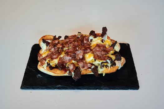 A bacon and cheese sandwich is on a black table. The sandwich is large and has a lot of bacon and cheese