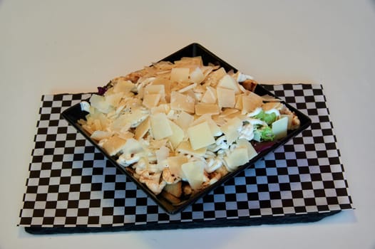 A plate of food with cheese and chicken on it. The plate is on a checkered tablecloth
