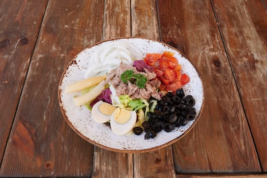 A plate of food with a variety of ingredients including tomatoes, olives, and eggs. The plate is on a wooden table
