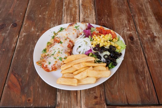 A plate of food with a piece of meat, a side of fries, and a salad. The plate is on a wooden table