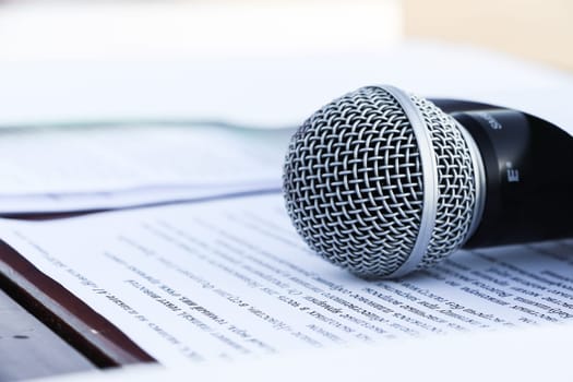 Microphone lies on pages with text on white background. Close-up. Soft focus. Concept of audio recording of prints, dubbing, listening. Hosting an event. Attributes of a concert presenter.