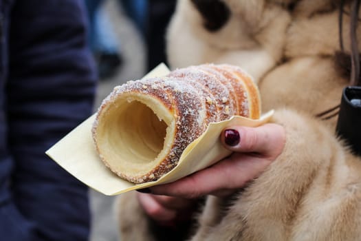 A woman dressed in a luxurious coat elegantly holds a delicious cake in her hand, enjoying its delicious aroma and taste. A close-up of a confectionery product