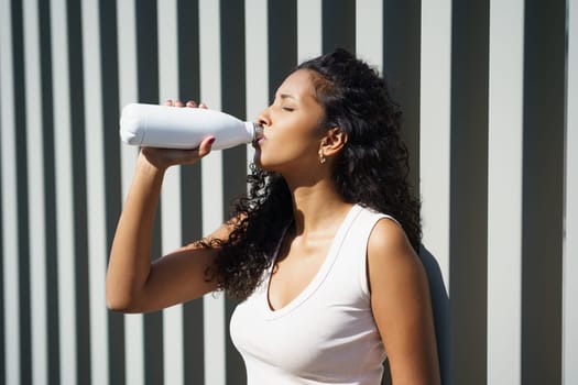 A vibrant and lively woman enjoys a refreshing drink, soaking in the warm sunlight. This moment highlights the vital importance of staying hydrated, prioritizing health and wellness every single day