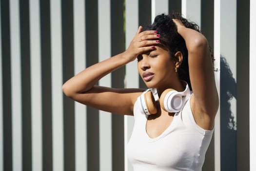 A young woman stands outdoors, wearing headphones, while expressing her emotional struggles against a backdrop that is distinctly modern and urban, reflecting contemporary life and its challenges